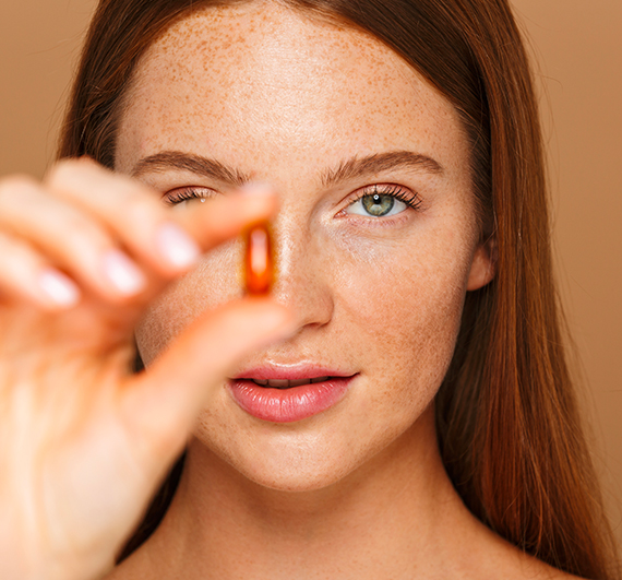 Jeune femme rousse à la peau éclatante tenant une gélule rouge de phytocéramides l Lipowheat™